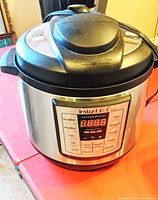 Front view of the Instant Pot Lux model stainless steel electric pressure cooker showing digital control panel and lid with safety valve.