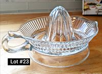 Photo of clear glass manual citrus juicer with ribbed base, reamer, handle, and pouring spout on a wooden surface