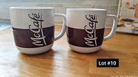 Photo of two wide white ceramic mugs with a thick dark brown band and McCafe logo on a wooden surface.