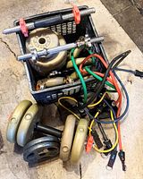 Photo shows two adjustable dumbbell bars with collars, four 5 lb weight plates, and four 2.5 lb weight plates arranged together with some wires and other miscellaneous items in a crate.