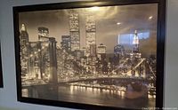 Framed black and white print depicting New York City skyline at night including the Twin Towers and Brooklyn Bridge, hung on wall.