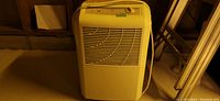 Older cream colored portable dehumidifier with air vent front grill and top mounted control panel in a storage or basement setting