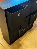 Black shelving unit with nine compartments filled with black removable cloth bins that have circular metal grommet handles.