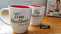 Two Tim Hortons mugs placed on a wooden table, showing front and partial side views of each mug.