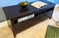 Photo of wooden TV stand showing top surface, two drawers below, and two open shelves with devices inside.