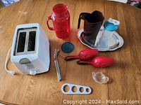 White 2-slice toaster, red milk bag container, red scoops, steel spaghetti measure, tea bag holder, red shaker cup, small plastic container, and silver serving tray.
