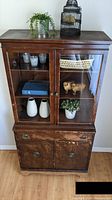 Front view of the vintage wood China cabinet showing glass doors on upper section and wooden doors with veneer damage on lower section.