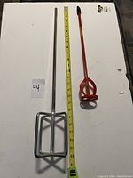 Photo showing two large paint mixers side by side with a measuring tape indicating lengths. One mixer has a chrome square paddle, the other a red circular helix paddle.