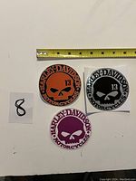 Three Harley Davidson motorcycle decals displayed on a flat surface with a measuring tape showing 4 inch size.
