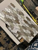 Six sheets of mosaic tiles laid out on a surface showing multi-colored metallic elongated hexagonal tiles reflecting light.