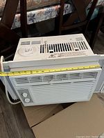 Front view showing air conditioner with measurement tape indicating width.