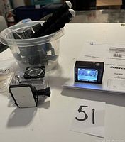 Photo showing action camera LCD screen, waterproof case, flexible tripod, and user manual