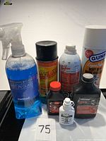 Top view of seven assorted car care and motor maintenance products including spray bottles, aerosols, and small treatment bottles on a white surface.