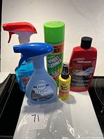 Photo shows five car care products on a black surface with a white backdrop and a paper marked '71'. Items include Windex glass cleaner, Febreze fabric refresher, Turtle Wax diamond wheel cleaner aerosol, Mothers speed polish, and Tuff Stuff multi-purpose cleaner.