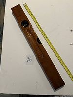 Top-down view of the wooden level, showing length and two bubble level windows, placed next to measuring tape for scale.