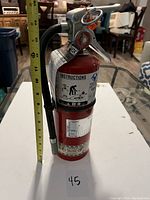 Full side view of red fire extinguisher with measuring tape showing approx. 14 inches tall, placed on white surface