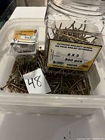Photo shows a clear bin with loose construction screws, alongside two labeled containers of screws. The container on the left is labeled '8x2 Construction Screws' and the larger container on the right is labeled '8 x 3 Outdoor Project Screw, 300 pcs, Yellow Zinc - Zine DI-Chromate, USCAN'.