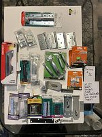 Top-down view of lot showing metal door handles, multiple hinges, lock clasps, and other hardware items arranged on a surface with handwritten note describing contents.