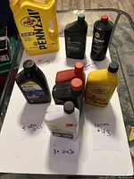 Photo shows a lot of nine automotive fluid containers arranged on paper with handwritten notes. Includes five new motor oil bottles, three 10W30 oils in front, a large yellow Pennzoil jug and other fluid bottles in back.