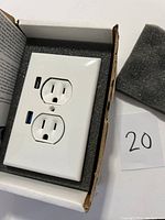 Front view of new white electrical receptacle with two standard outlets and two USB ports in packaging.