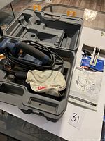 Ryobi electric hand planer placed inside the molded hard plastic carry case, with power cord coiled, dust collection bag, and instruction manual laid out.