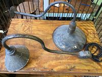 Photo showing both aged metal lights on wooden surface, highlighting the curved arm and different shade sizes.