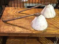 Two aged metal scoop lights on wooden surface showing rusted arms and white conical shades.