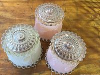 Three glass shades on a wooden surface, showing hobnail edges and decorative tops.