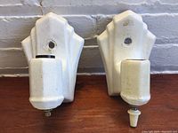 Front view of white ceramic Art Deco wall sconces showing the stepped backplate and bulb socket areas.