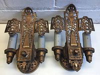 Front view of both sconces showing ornate cast metal design, dual candle sockets