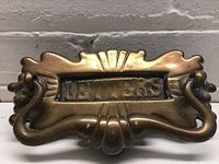 Close-up frontal view of the Art Nouveau brass mail slot showing embossed lettering and the ornate handle.