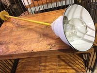 Full view of the industrial light fixture showing the white enamel shade, yellow pipe, and mounting plate, laid on a wooden surface.