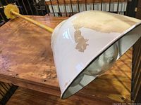 Side angle view of the white enamel shade showing large paint chipping and the long yellow mounting pipe.