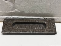 Front view showing the embossed 'LETTERS' text and decorative border on the metal mail slot.
