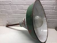 Side angled view showing wide green enamel shade with red stripe and original glass globe inside.