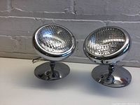 Pair of round Opololite lights side by side on white surface, showing chrome finish and clear lenses