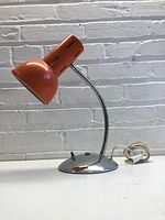 Full view of the orange task light showing the shape, color, and flexible neck with chrome base.