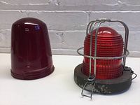 Two red glass signal globes side by side on a white surface with brick wall background
