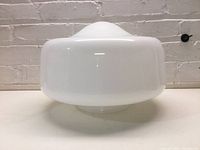 Side view of milk glass schoolhouse globe light shade with smooth white finish against a brick wall background.