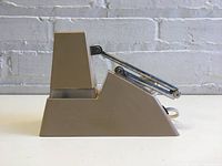 Side view of the tan folding desk lamp showing compact folded position against a white brick wall background.