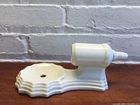 Front view of the vintage white ceramic sconce showing scalloped round base with mounting hole and cylindrical candle or light holder.