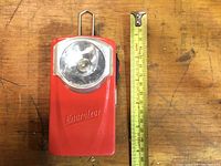 Front view of vintage red Energizer pocket light with clear lens and bulb socket, placed next to a measuring tape for scale.