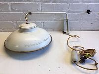 White adjustable weighted pendant light laid on a white surface with visible cord, plug, and wall mount bracket.