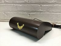 Brown weighted shelf light with gold decorative accents shown from angled front view on white surface with a white brick background.