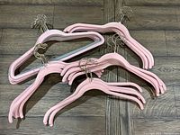 Photo of a pile of 43 pink velvet hangers with gold hooks on a wooden floor.