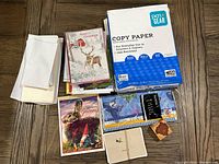 Overview photo showing assorted cards, envelopes, tissue papers, and copy paper pack on wooden surface.