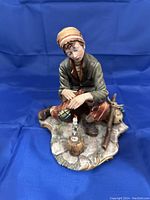 Front view of the porcelain figurine showing the hobo seated with hands extended towards the lit candle in a bottle holder on a rustic stone base.