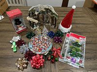 Overview of Christmas decor lot including nativity scene, snowman nightlight box, Santa gnome hat, decorative bows, cat plate, and window clings on wooden table.