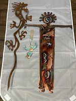 Photo of two metal art pieces laid on white cloth. Copper shaman figure with colorful patina and rusted steel dragon with textured surface by Ray Rizzo.