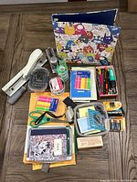 Front view of office supplies lot arranged on wooden surface including binder, stapler, pens, scissors, labels, batteries, and more.